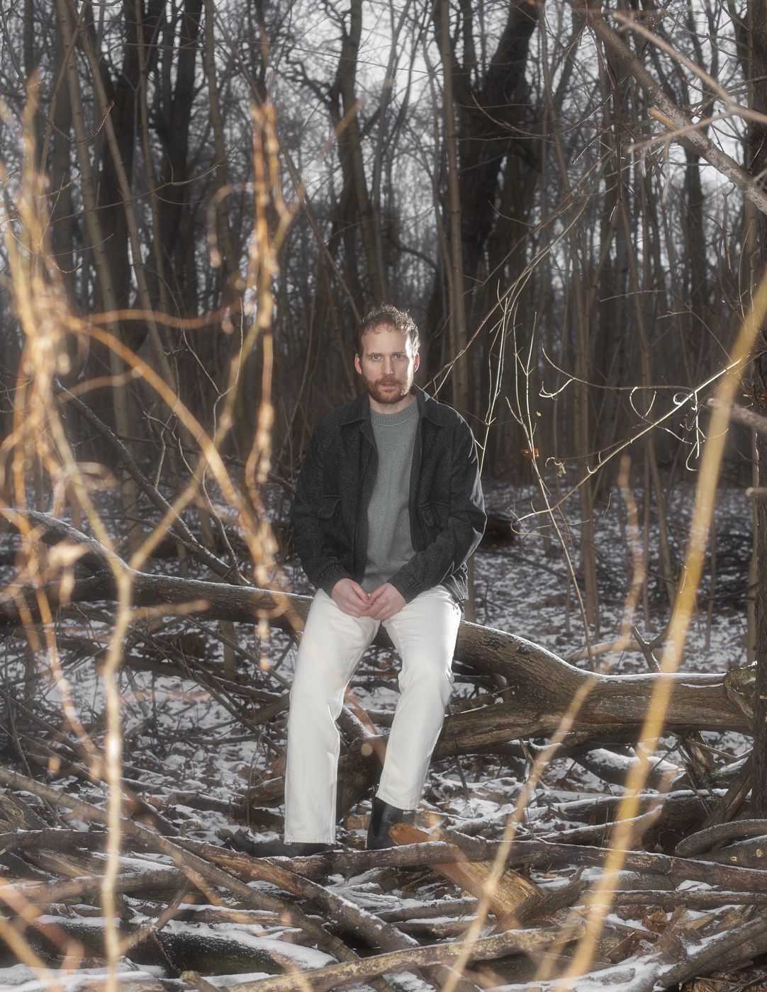 Piotr Kurek seated on a fallen tree in a snowy wood